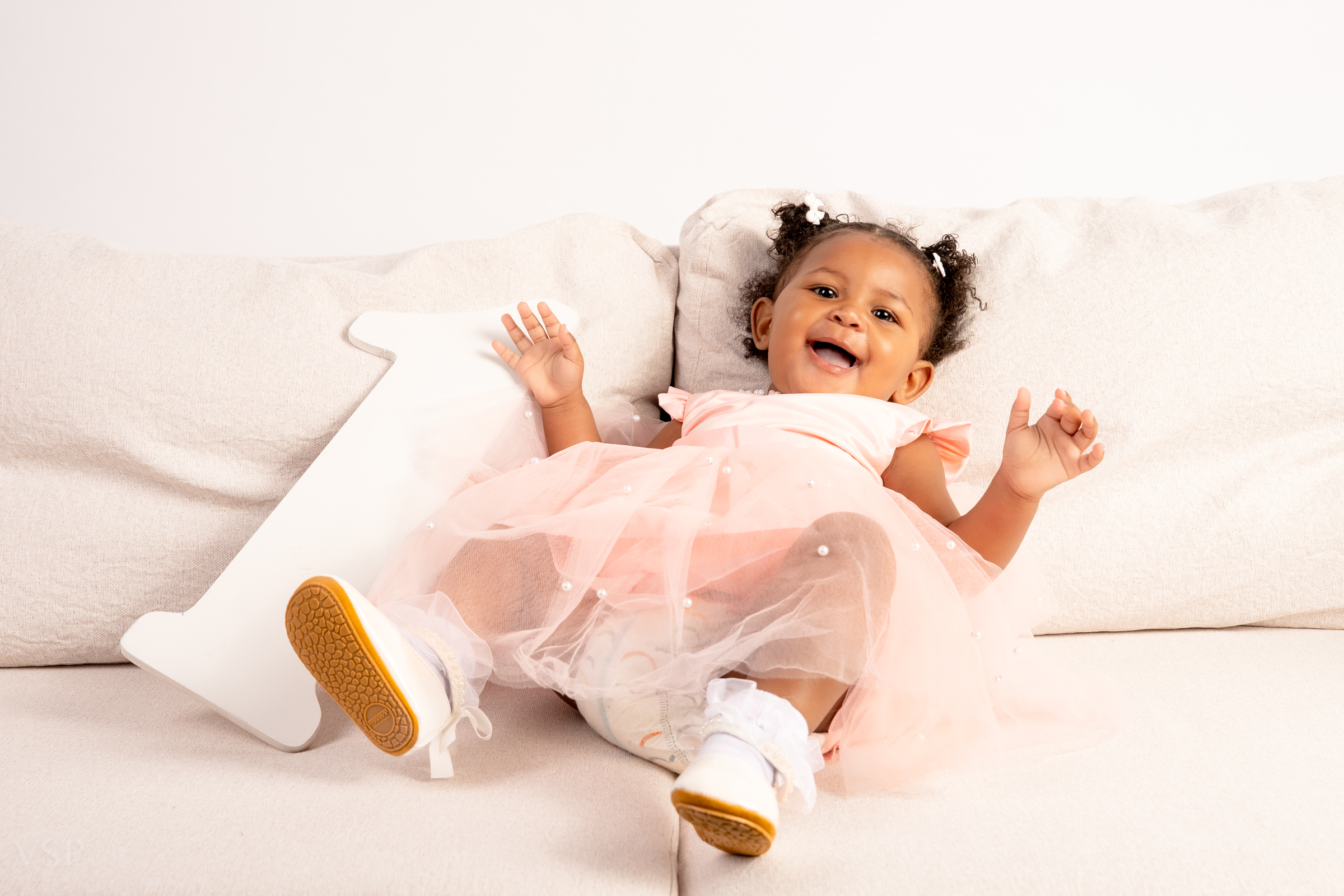 Candid moment of baby girl enjoying first birthday photoshoot in Denver studio capturing playful expression and joyful celebration