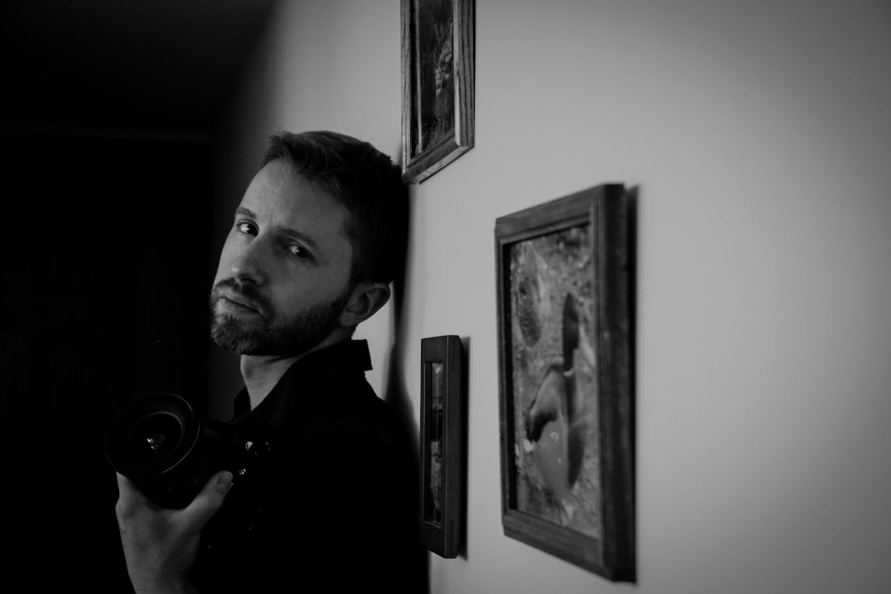 A contemplative male photographer holding a camera in a black and white composition.