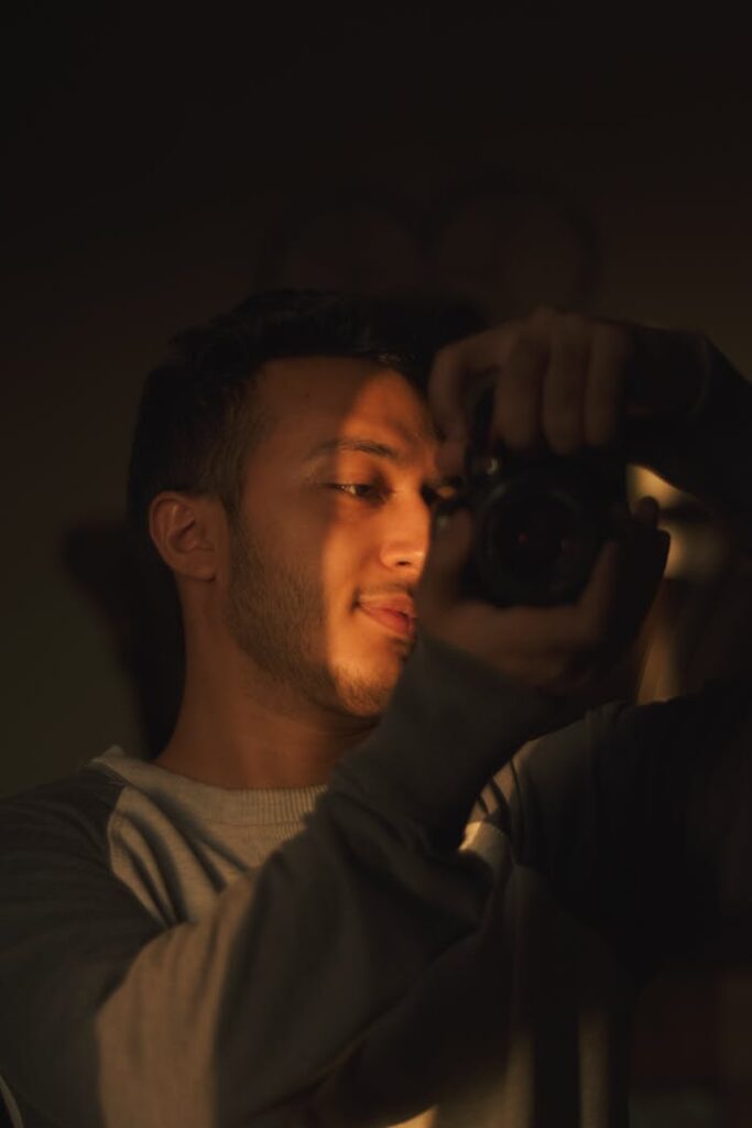 A candid portrait of a male photographer capturing a creative moment indoors, highlighted by warm lighting.