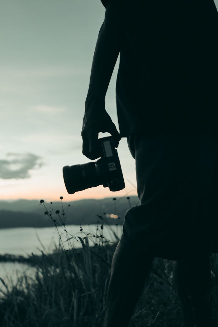 A photographer holding a camera in silhouette against a serene sunset backdrop.