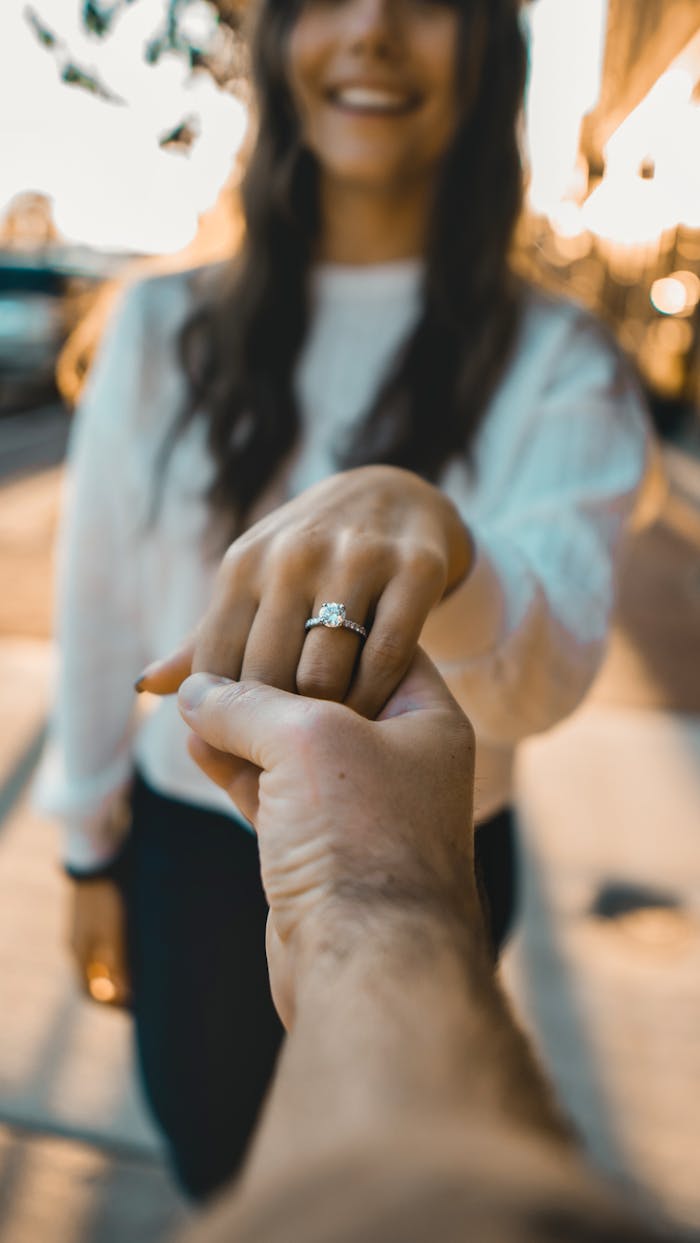 Capture the moment of a romantic engagement proposal with a sparkling diamond ring and holding hands.